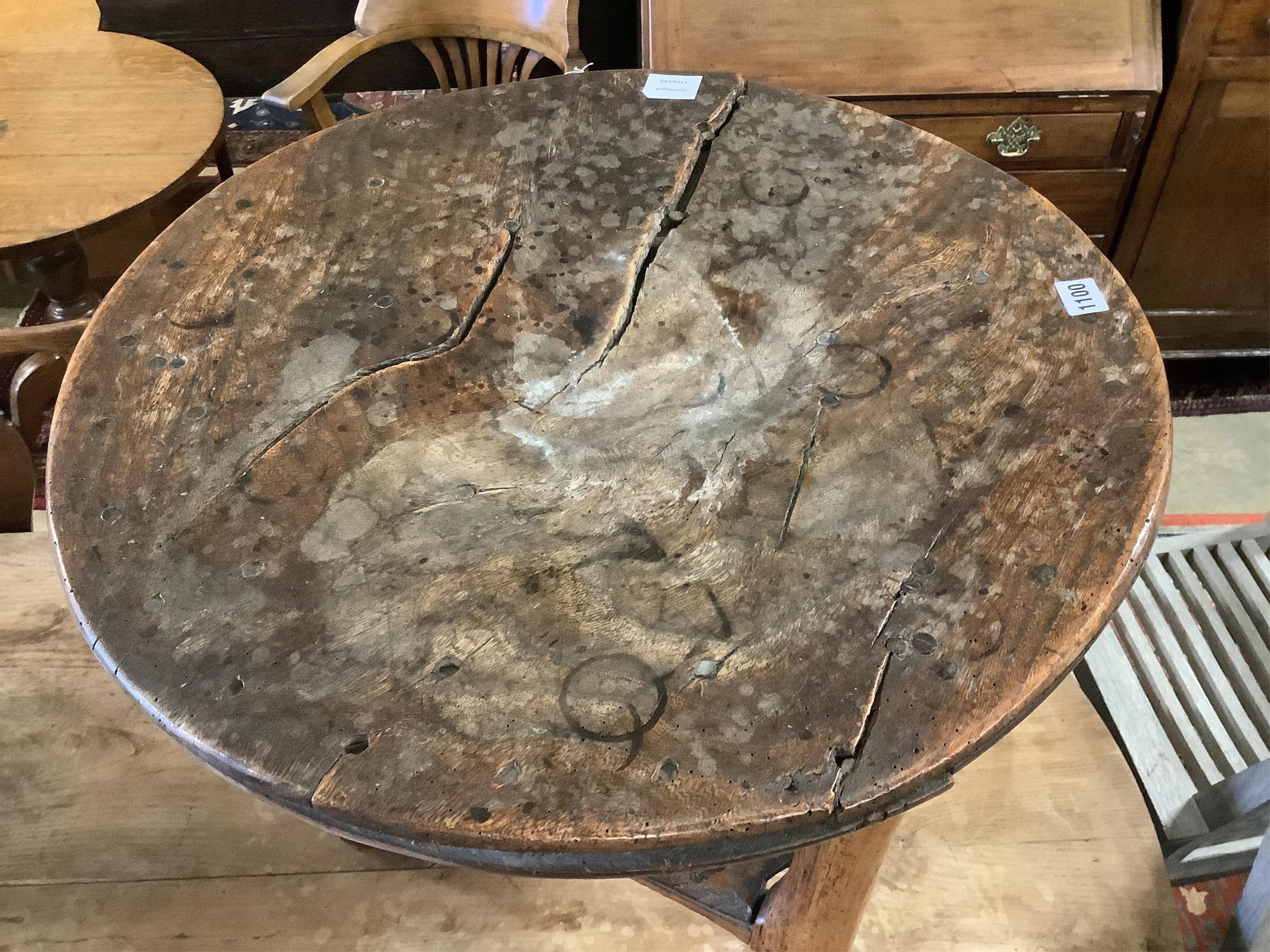 An 18th century elm cricket table, width 63cm, height 64cm. Condition - extensive splitting and old patches and repairs to the top, legs probably reduced, but full of character